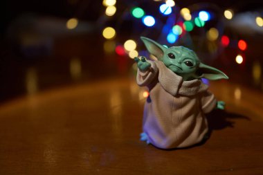 Ekim 2021: Bebek Yoda, Yıldız Savaşları 'nın aksiyon figürlerinden biri masada duruyor. Çok renkli bir çelengin ışıklarıyla siyah arka plan. Yüksek kalite fotoğraf