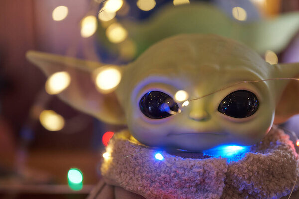 October, 2021: Baby Yoda, an action figures of Star Wars standing on the table. Black background with lights from a multi-colored garland