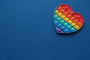 Kalp, silikon renkli anti-stres oyuncağı mavi arka planda. Patlayan baloncuğa tıklayın. Gamzeli basit bir oyuncak. Romantizm konsepti, aşk, hediye, sevgililer günü, tatil