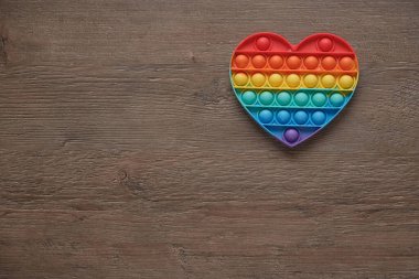 Kalp, silikon renkli anti-stres oyuncağı tahta arka planda. Patlayan baloncuğa tıklayın. Gamzeli basit bir oyuncak, yakın plan. Romantizm konsepti, aşk, hediye, sevgililer günü, tatil