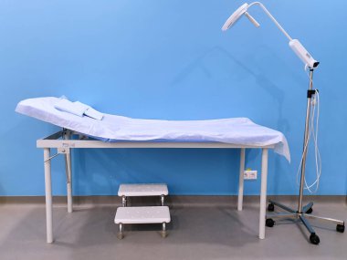 Mavi arka planda boş bir sağlık yatağı, yakınlardaki merdivenler, muayene odası. terapi. Modern tıp teknolojileri ve tıbbi ekipmanlar.