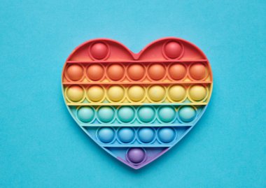 Yakın plan. Kalp, silikon renkli anti-stres oyuncağı mavi arka planda. Patlayan baloncuğa tıklayın. Gamzeli basit bir oyuncak. Romantizm konsepti, aşk, hediye, sevgililer günü, tatil