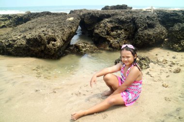 Genç Asyalı kızlar plajda beyaz kumlu ve kayalık arka planda mayo ve gözlüklerle poz veriyorlar.