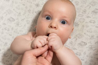 Bebek oynuyor, ellerini yiyor ve kameraya bakıyor.