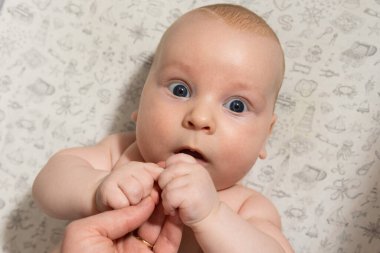 Bebek oynuyor, ellerini yiyor ve kameraya bakıyor.