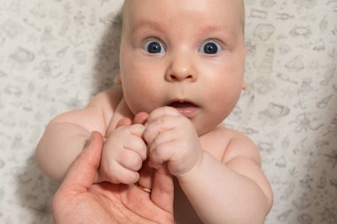 Bebek oynuyor, ellerini yiyor ve kameraya bakıyor.