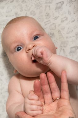 Bebek oynuyor, ellerini yiyor ve kameraya bakıyor.