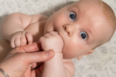 Bebek oynuyor, ellerini yiyor ve kameraya bakıyor.