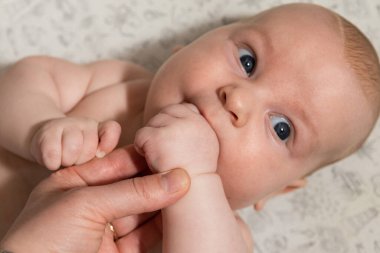 Bebek oynuyor, ellerini yiyor ve kameraya bakıyor.