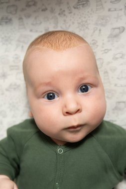 Üç aylık, mavi gözlü, yeşil elbiseli bir bebeğin yakın plan portresi.