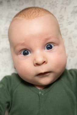 Üç aylık, mavi gözlü, yeşil elbiseli bir bebeğin yakın plan portresi.