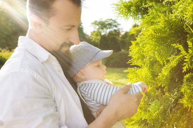 Yeşilliğin arka planında oğlunu kollarına alan bir baba.