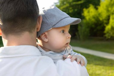 Yeşilliğin arka planında oğlunu kollarına alan bir baba.