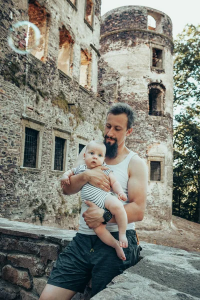 A six-month-old baby in the arms of a father against the backdrop of an old castle