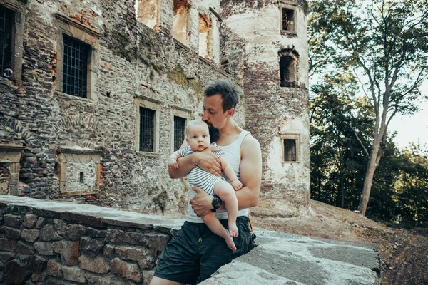 A six-month-old baby in the arms of a father against the backdrop of an old castle