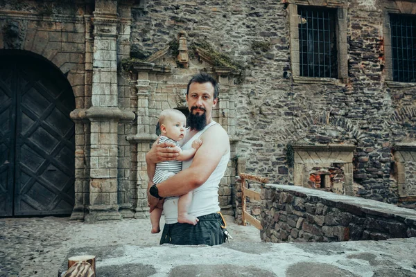 A six-month-old baby in the arms of a father against the backdrop of an old castle
