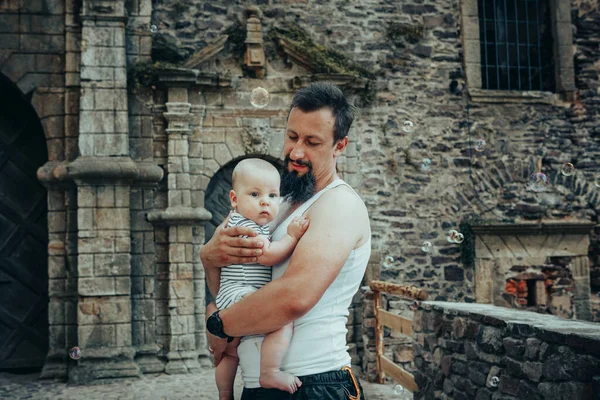 A six-month-old baby in the arms of a father against the backdrop of an old castle