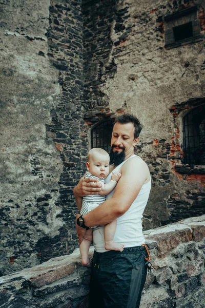 A six-month-old baby in the arms of a father against the backdrop of an old castle