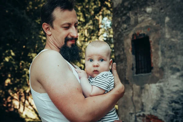 A six-month-old baby in the arms of a father against the backdrop of an old castle