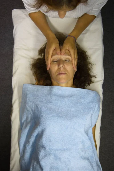 Yüz masajı. Düz yatıyordu. Masöz yüz masajı yapıyor. Parmaklarını kadının alnına vurur..