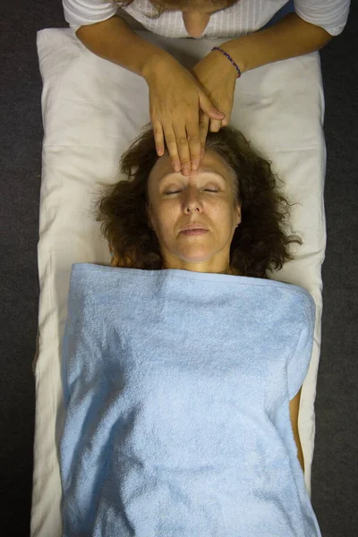 Yüz masajı. Düz yatıyordu. Masöz yüz masajı yapıyor. Parmaklarını kadının alnına vurur..