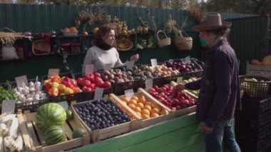 Marketten kırmızı elma almak. İki kamerada çekim yapmak. 2 Shot. Bir adam pazardan elma alır. Bir kadın ona plastik bir torba verir ve içine elma koyar..