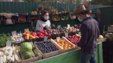 Marketten meyve ve sebze almak. İki kamerada çekim yapmak. 2 Shot. Bir adam pazarda elma, portakal, patates ve pancar seçiyor. Tezgahın arkasında bir kadın satıcı var..