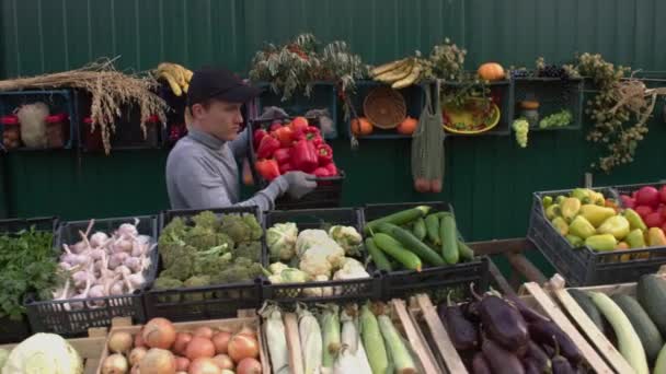 農家の市場で赤ピーマン 男性の営業担当者がカウンターに唐辛子の箱を置きます カメラは 野菜の様々なボックスに沿ってスムーズに移動します — ストック動画