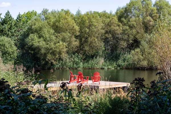 Ontario, Kanada 'da bir göldeki rıhtımda üç kırmızı Muskoka Adirondack sandalyesi. Arkaplanda orman.