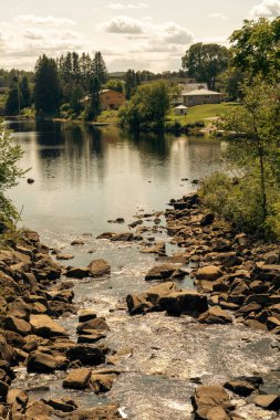 Güneş ışığında parıldayan kaya ve ayaklı nehrin dikey görüntüsü. Arka plandaki evler. Kuzey Ontario, Kanada. Eski. 
