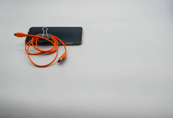 Telefon Komórkowy Ciemnym Ekranem Jasnym Pomarańczowym Kablem Ładowania — Zdjęcie stockowe