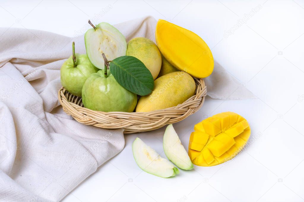 Fresh green guava and ripe yellow mango fruits in bamboo basket isolated on white background. Exotic tropical fruits in wicker basket and sliced fruit in front of basket, healthy food, diet nutrition