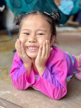 Sevimli bir çocuk olan Asyalı bir kadının portresi. Kocaman gülümseyen ve kameraya bakan mutlu küçük bir kız. Evde poz veren pozitif çocuk, mutlu ve neşeli bir çocuk.