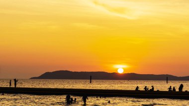 Okyanusun parlak turuncu suları üzerinde parlayan renkli günbatımı manzarası. Koh Larn Sahili 'nde gün batımında yürüyen, rahatlatan ve fotoğraf çeken turist silueti.. 