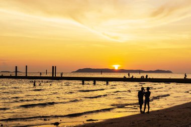 Okyanusun parlak turuncu suları üzerinde parlayan renkli günbatımı manzarası. Koh Larn Sahili 'nde gün batımında yürüyen, rahatlatan ve fotoğraf çeken turist silueti.. 