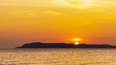 Okyanusun parlak turuncu suları üzerinde parlayan renkli günbatımı manzarası. Pattaya 'daki Koh Larn Sahili' nde güzel tropikal günbatımı olan Siluet Cennet Adası. Günbatımının arka planında yumuşak bir odak