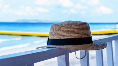 Plajın yanındaki restoranın balkonunda bulanık mavi deniz arka planına yakın plan hasır şapka. Esmer kadın şapkası rahatlatıcı ya da dinlendirici arka plan, seçici odaklanma. Yaz tatili kavramı