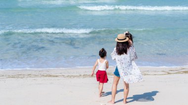 Gündüz vakti kumsalda oynayan anne ve kız çocuklarının arka görüntüsü. Aile babası, yaz tatilinde tropik plajda yürüyen kız çocukları. Fotokopi alanı olan aile tatili fikri