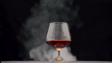 Sert bir alkolik içkisi. Viski, brendi, bardakta konyak ve puro dumanı.