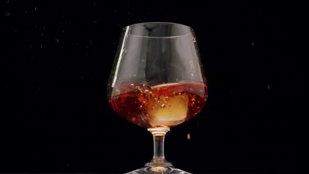Isbitar faller i stark alkoholhaltig dryck, galss med hälla kognak, Whiskey — Stockvideo