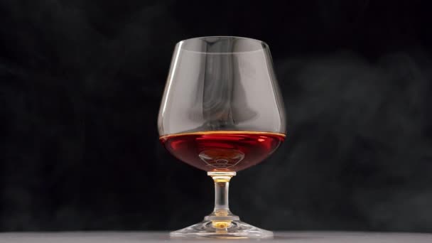 Une goutte de brandy tombe dans un verre d'alcool fort sur fond noir — Video