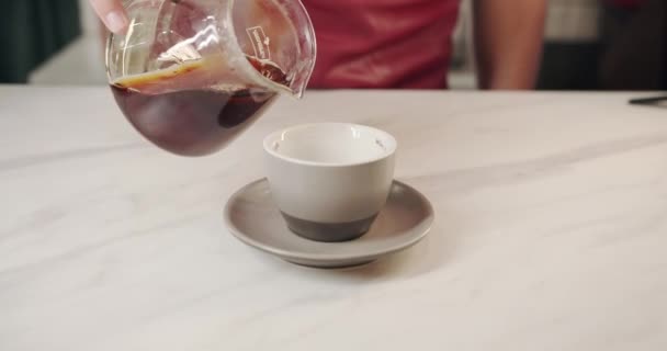 Barista giet in een transparante kom de koffie bereid volgens de V60 techniek — Stockvideo