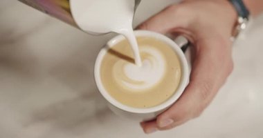 Barista iş yerinde, bir fincan koyu kahve yapıyor, kahvede kalp yapıyor.