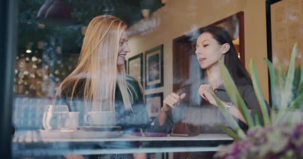 Två vackra och glada tjejer kopplar av, dansar och pratar på caféet — Stockvideo