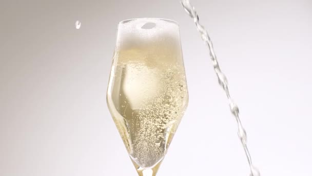 Пляшку шампанського наливають у ігристе скло на білому тлі — стокове відео