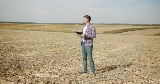 Um jovem agricultor no meio do campo, usando um tablet, agricultura moderna — Vídeo de Stock