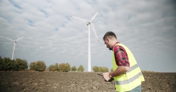 El ingeniero va a los molinos de viento con la tableta en la mano — Vídeos de Stock