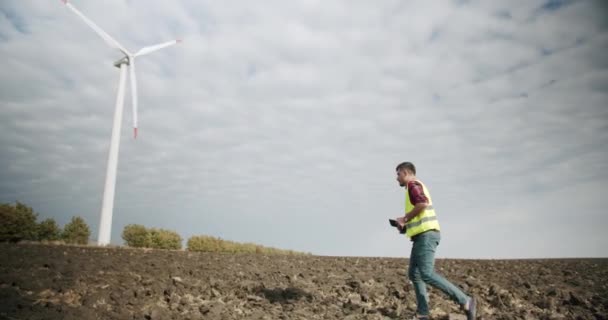 El ingeniero va a las turbinas de los molinos de viento con la tableta en la mano — Vídeo de stock