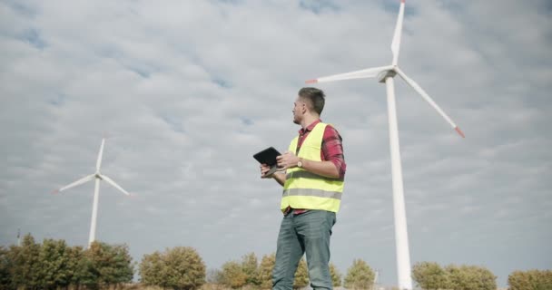 Young Engineer met tablet in de hand kijkt achter en werkt aan elektrische turbines — Stockvideo