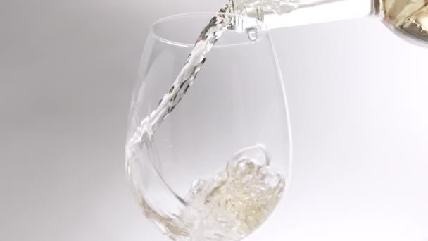 Выливание белого вина из прозрачного бокала в бокал на белом фоне — стоковое видео